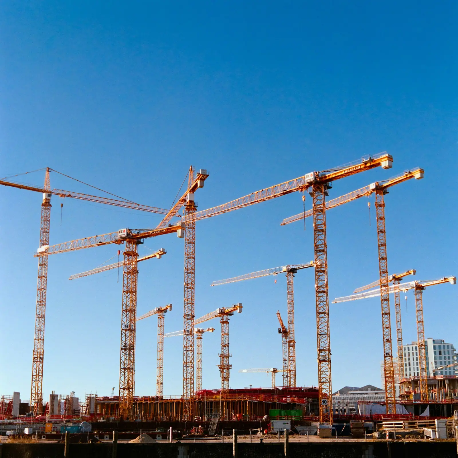 Baustelle mit zahlreichen Kränen vor blauem Himmel